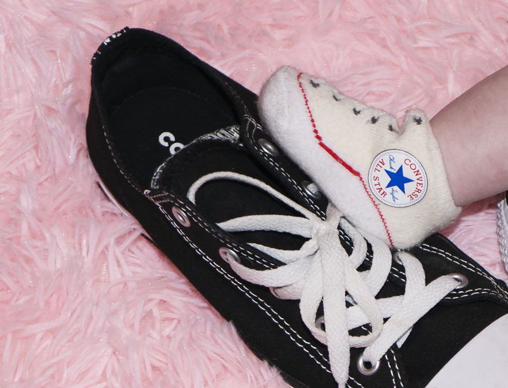 A baby wearing a pair of converse shoes on a pink carpet.
